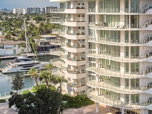 White curved hotel by a marina with glass balconies and palm trees amid boats and calm water