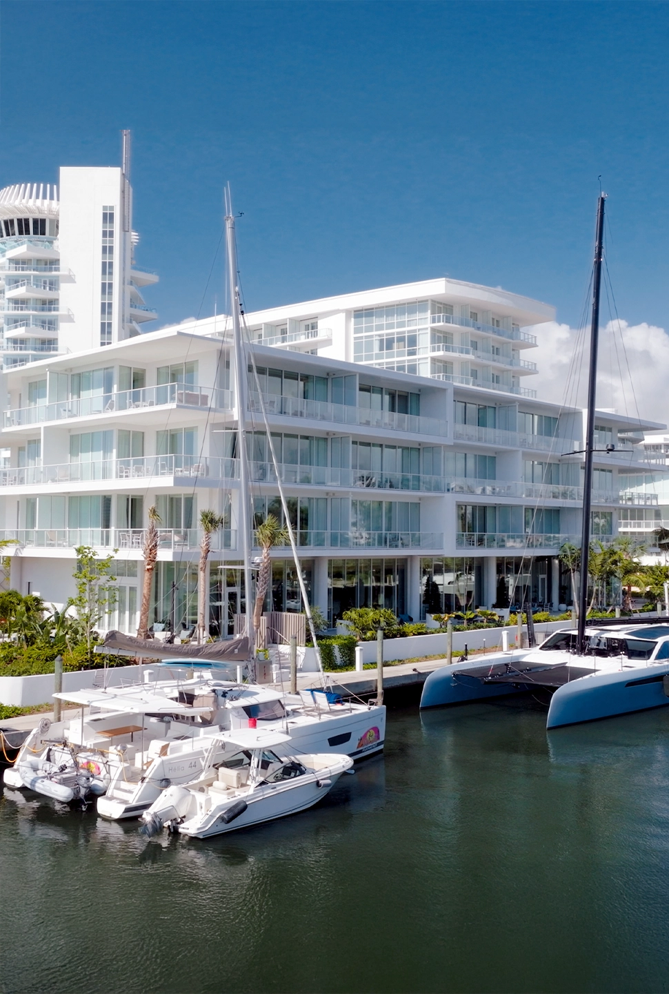 White modern condo building along a marina with docked sailboats and a blue sky above.